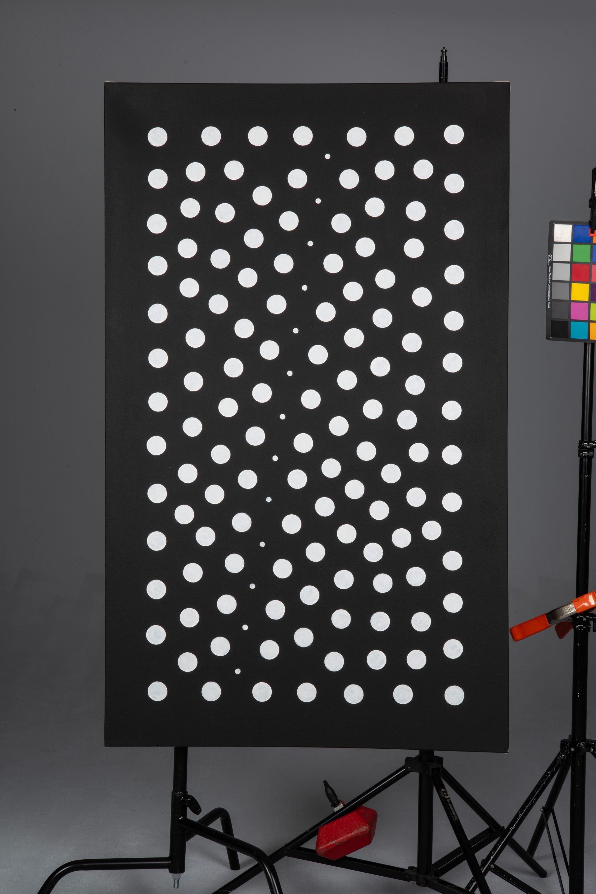 Black board with evenly spaced white circular dots, shown on a stand in a studio setting.