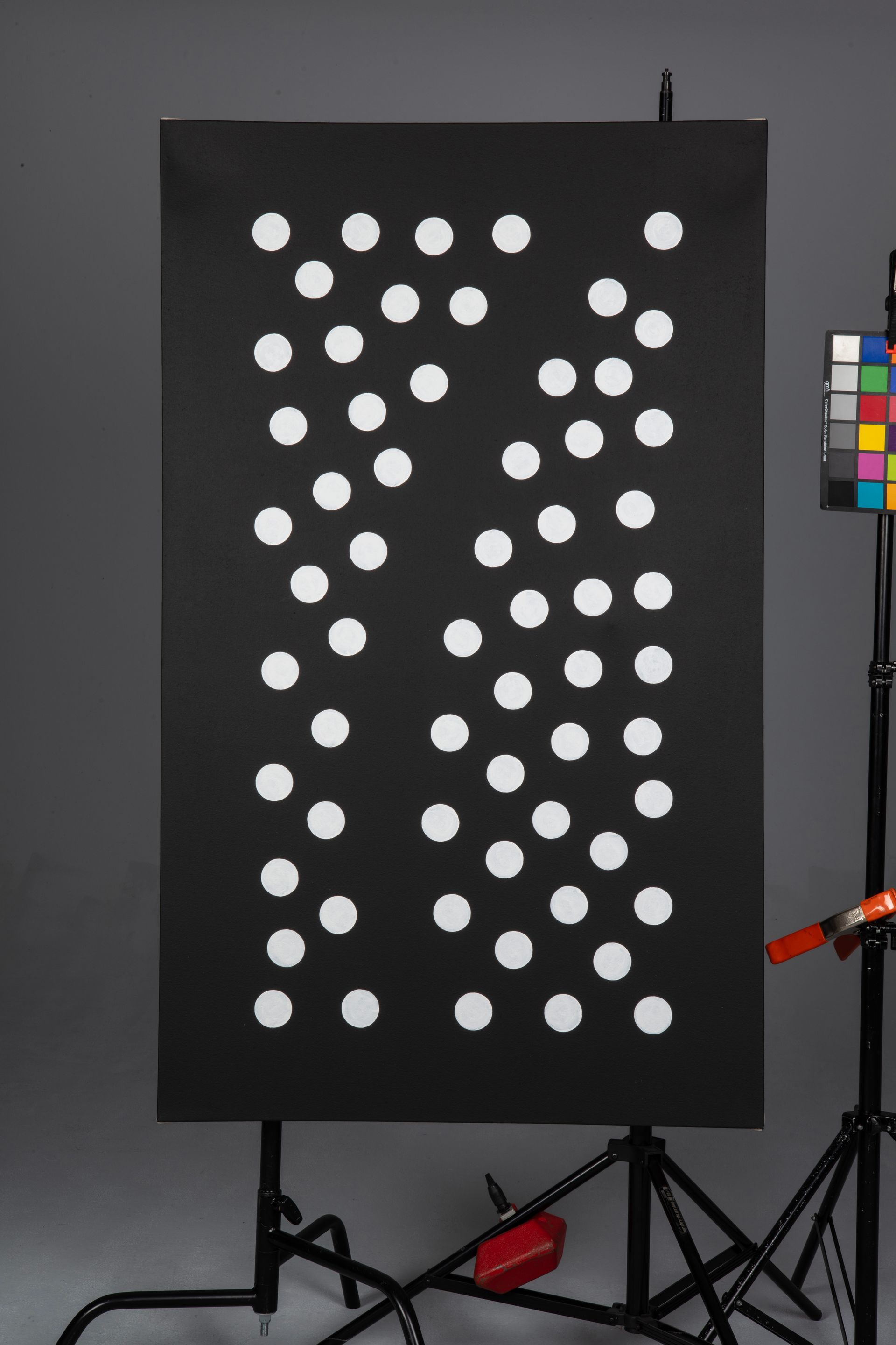 Black board with many white circular dots in a patterned grid, beside studio equipment and a color chart.