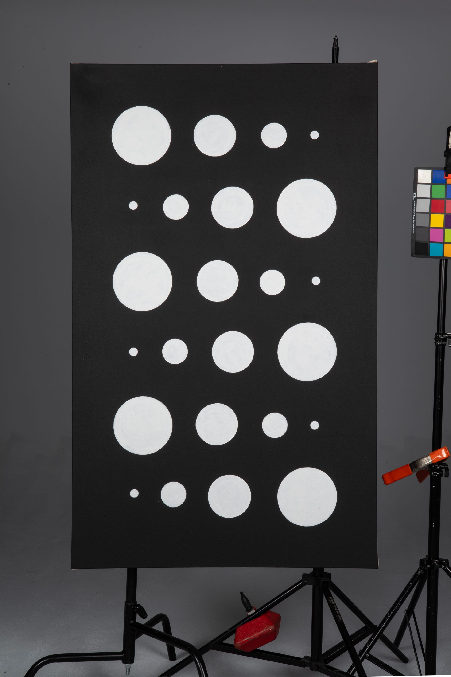 Black test chart with rows of white circles of varying sizes on a stand in a studio setup