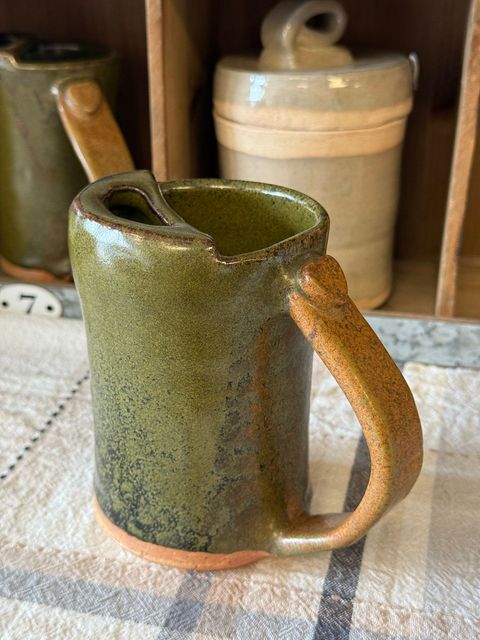 A green mug with a wooden handle is sitting on a table.