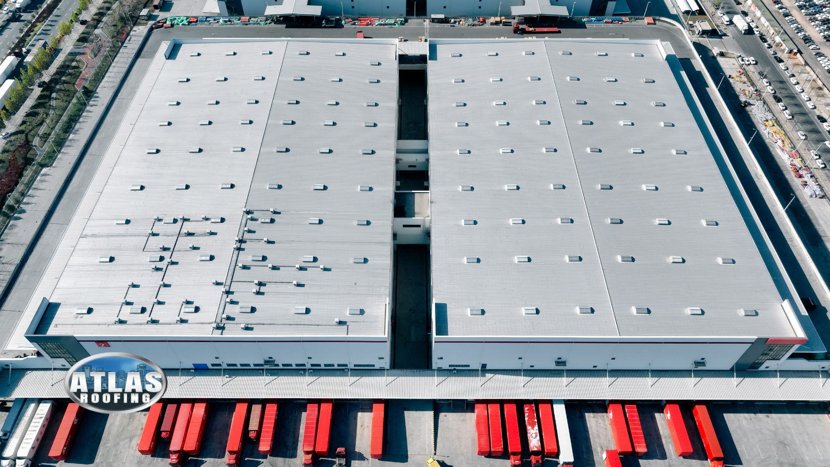 Aerial view of large warehouse with red loading docks and many vehicles.