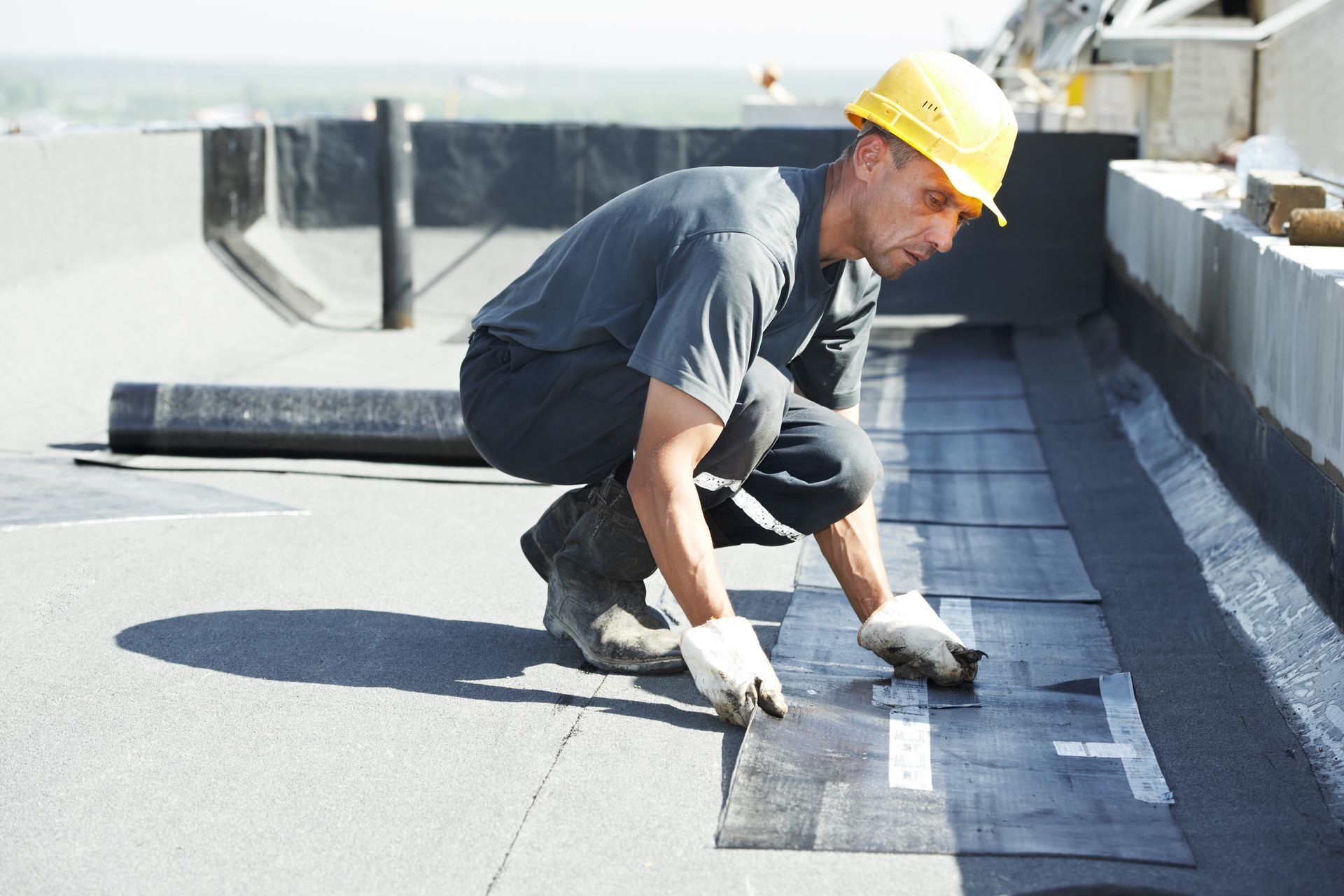 A man wearing a hard hat is working on a roof.