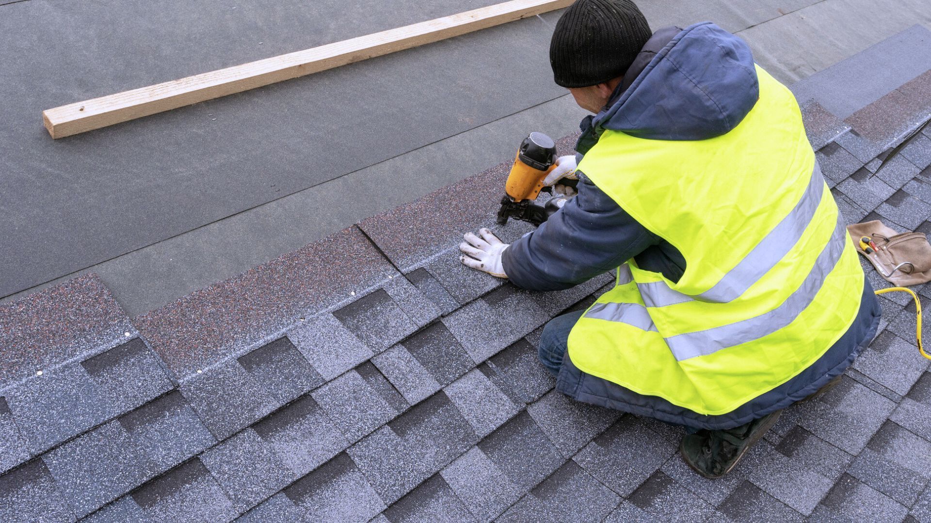 A man in a yellow vest is working on a roof.