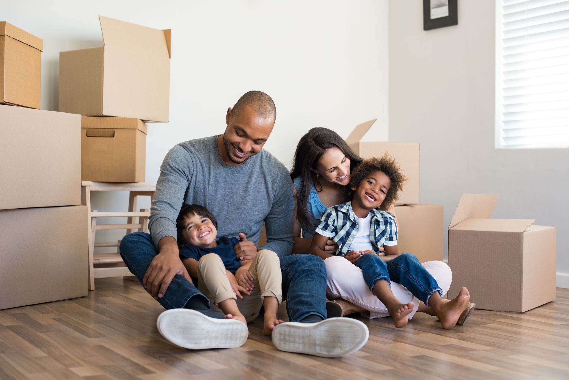 Family of four smiling, sitting on floor in new home with moving boxes.