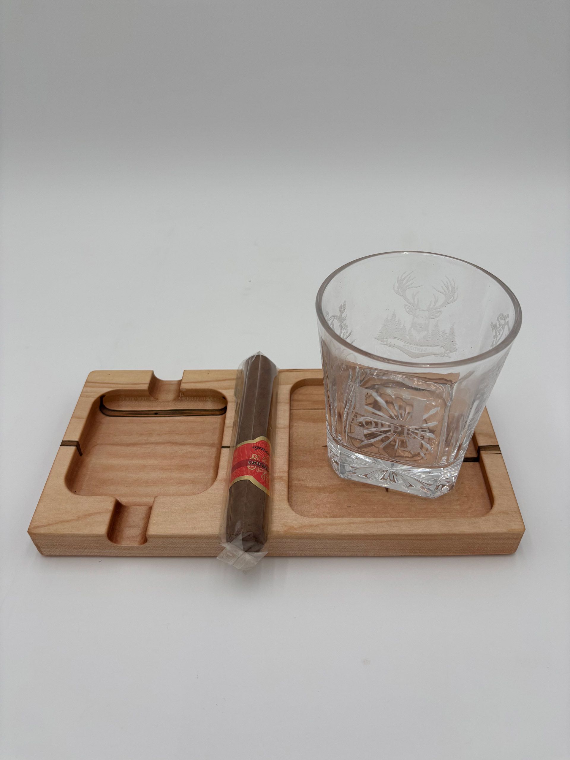 Wooden ashtray holding a cigar, next to a glass of water with ice against a white backdrop.