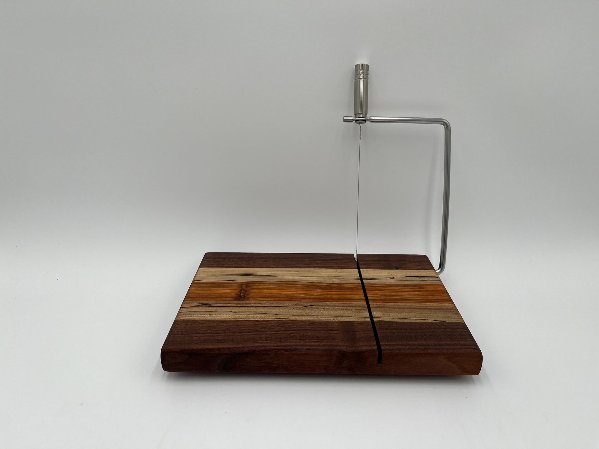 A wooden cutting board with a metal handle on a white surface.
