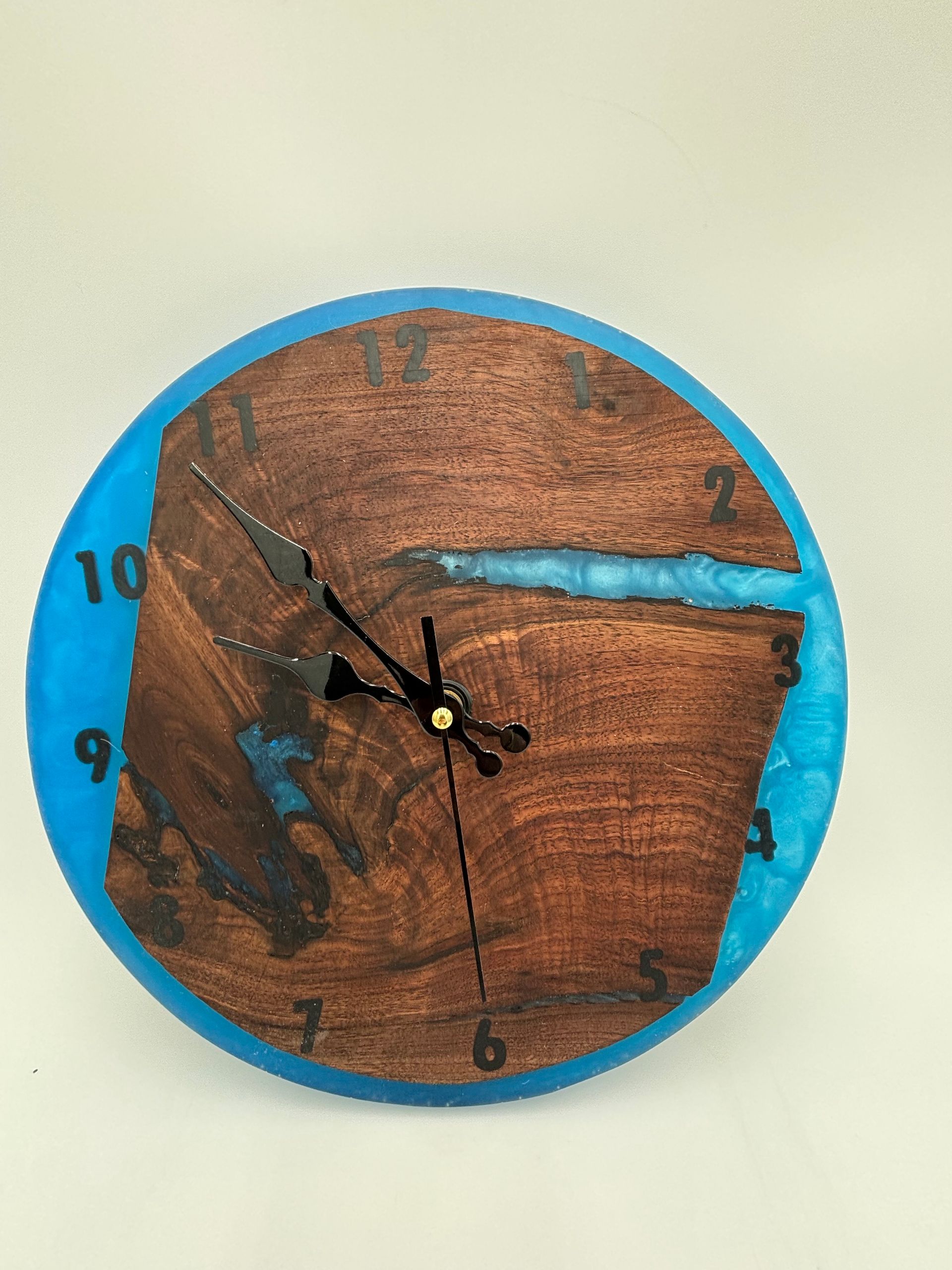 Clock made of wood and blue resin; black clock hands; numbers around the edge.