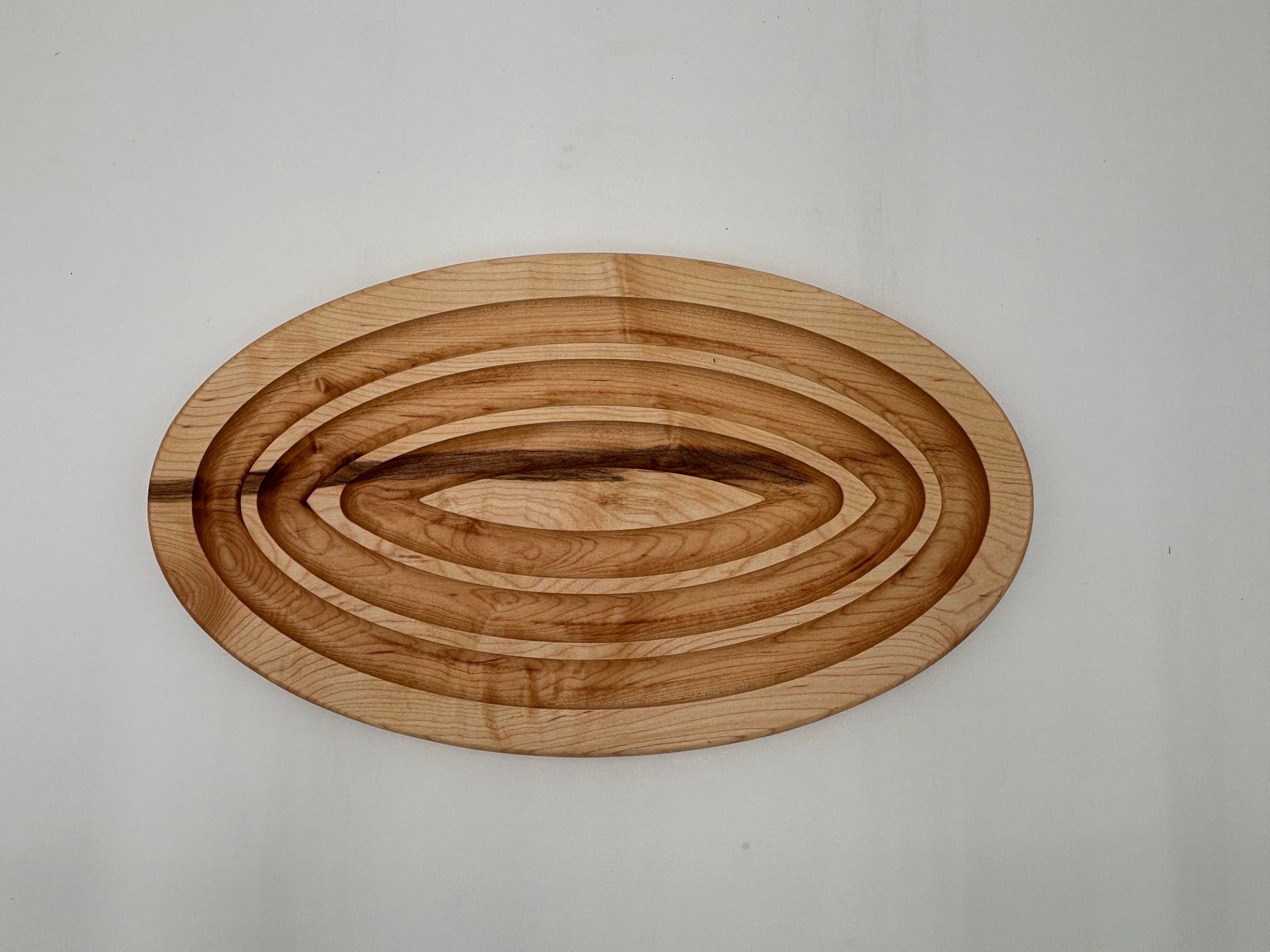 Oval wooden serving tray with concentric grooves.