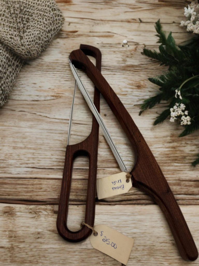 Two wooden cheese slicers with tags on a wooden surface.