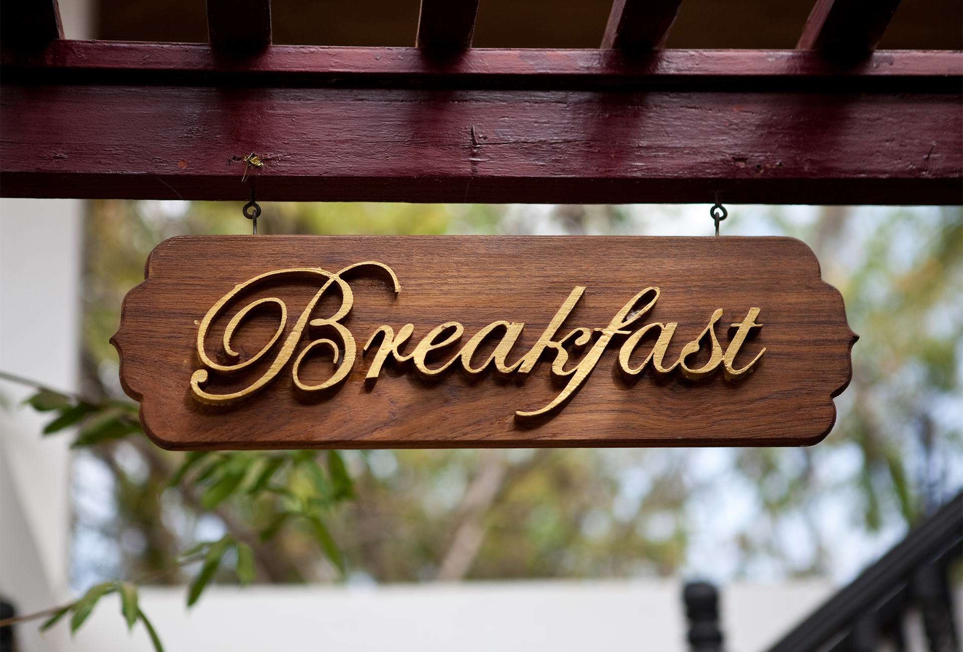 A wooden sign that says breakfast is hanging from a pergola