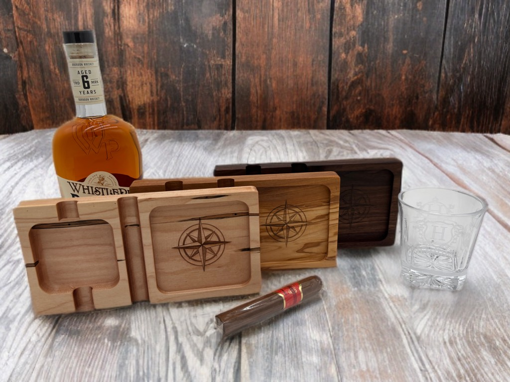 Wooden cigar ashtrays with a whiskey bottle, cigar, and a glass on a wooden surface.