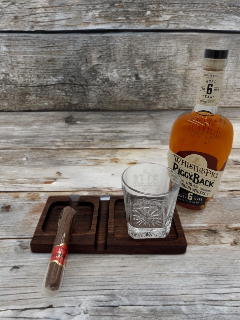 Whiskey, glass, and cigar on a wooden tray with a bottle of Pinhook Bourbon against a wooden background.