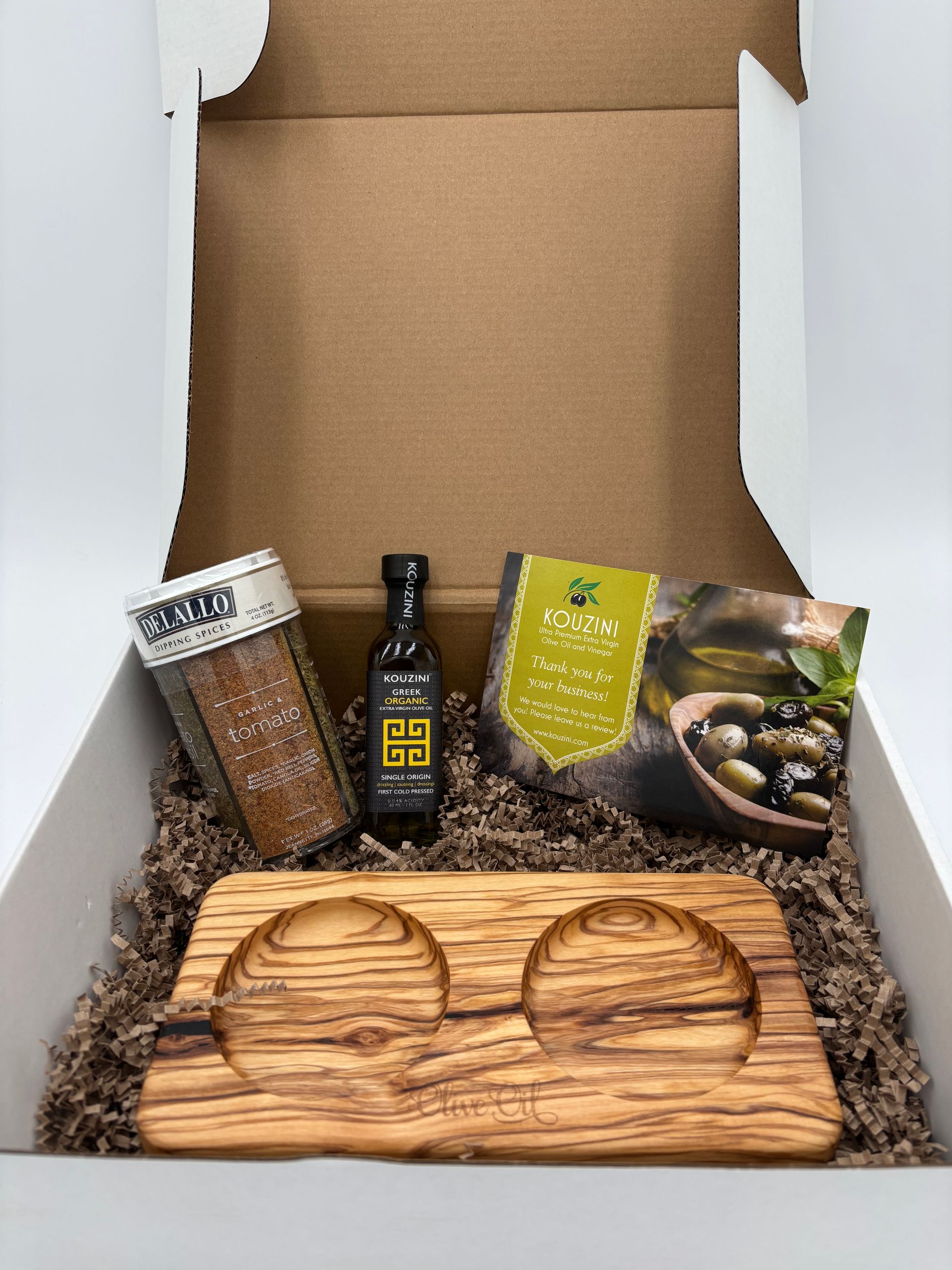 Olive oil gift box with spices, olives, oil bottle, and a wooden dipping tray.