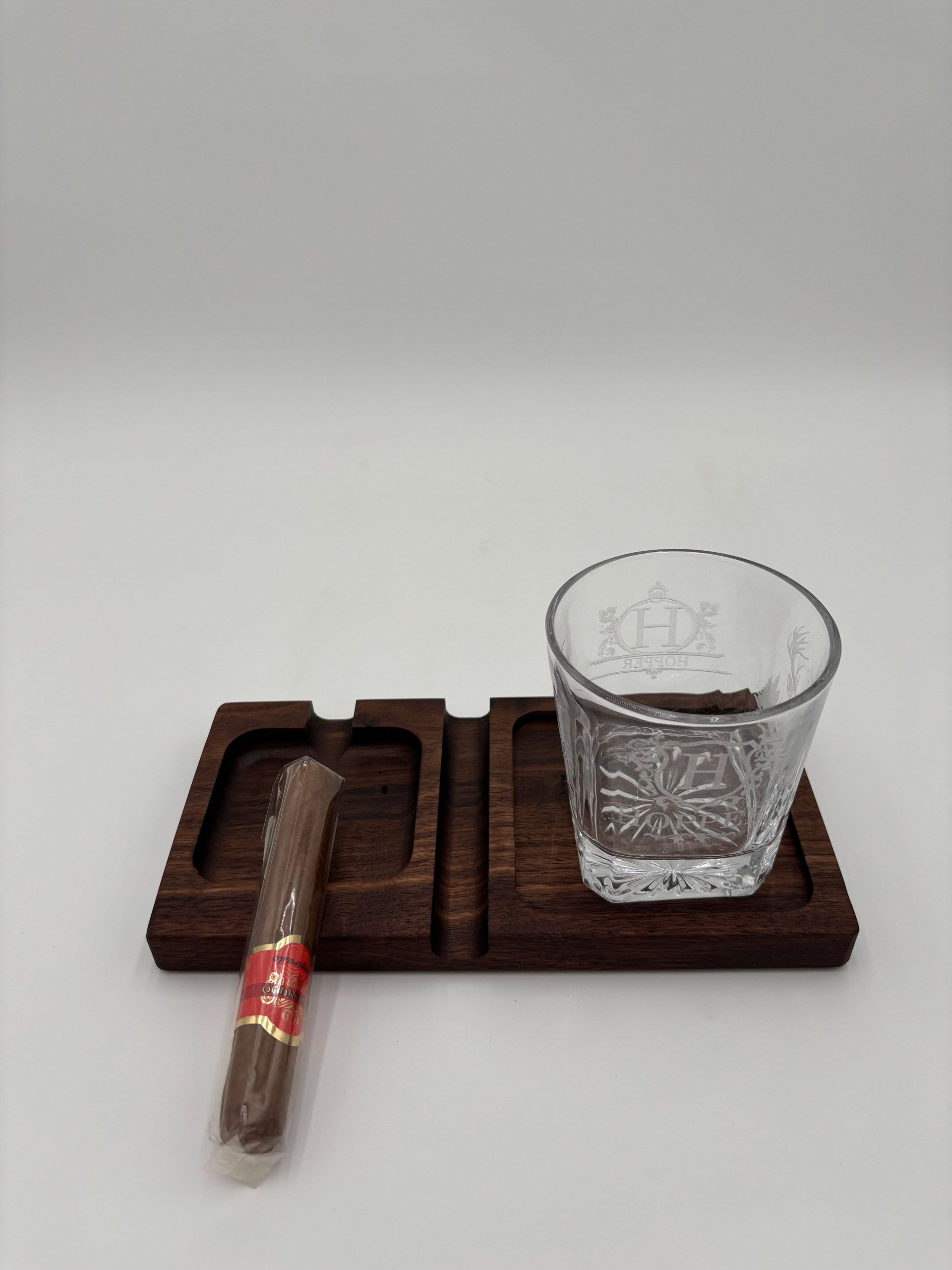 Dark wood cigar and whiskey tray with cigar, and decorative glass.