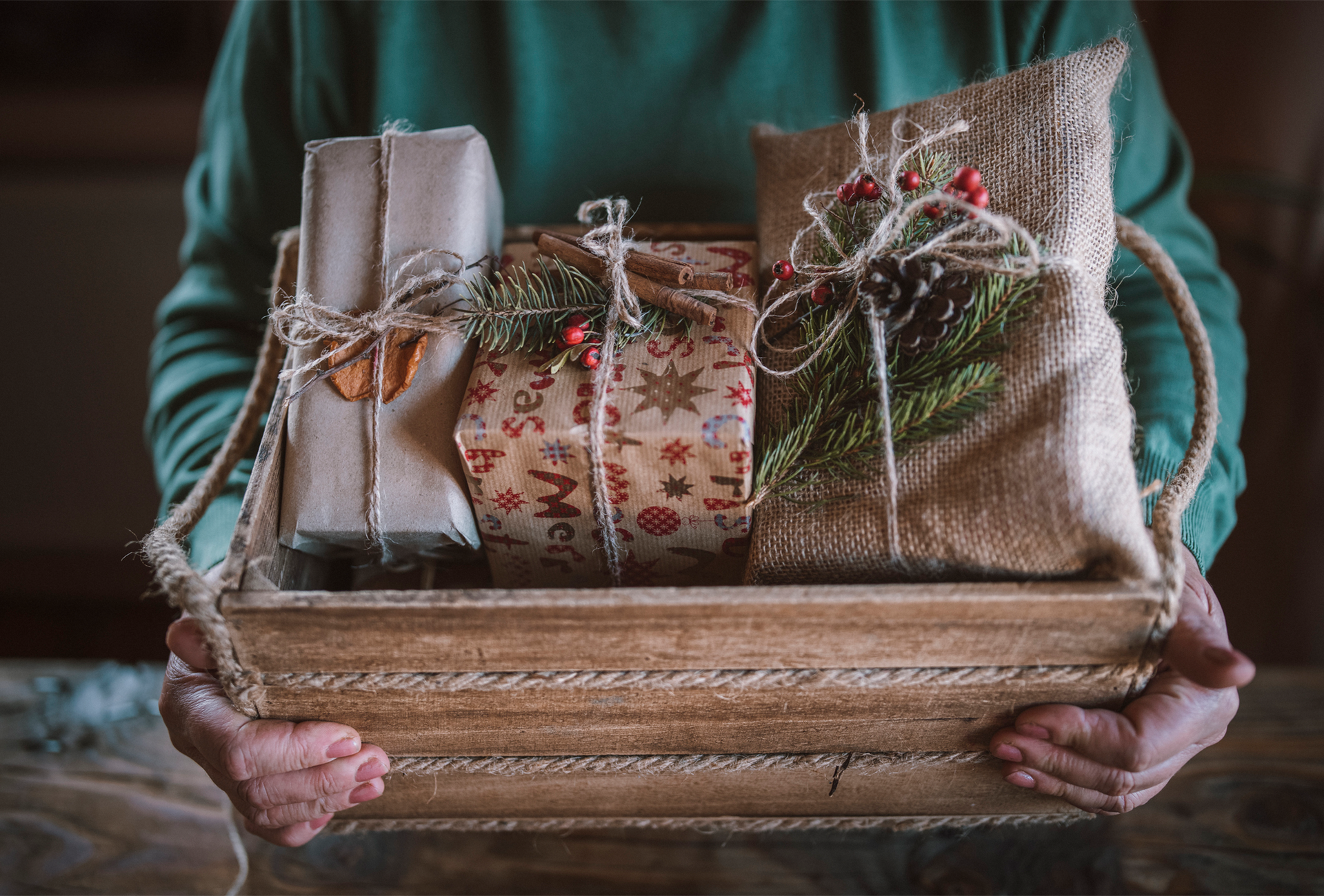 A person is holding a wooden basket filled with christmas presents