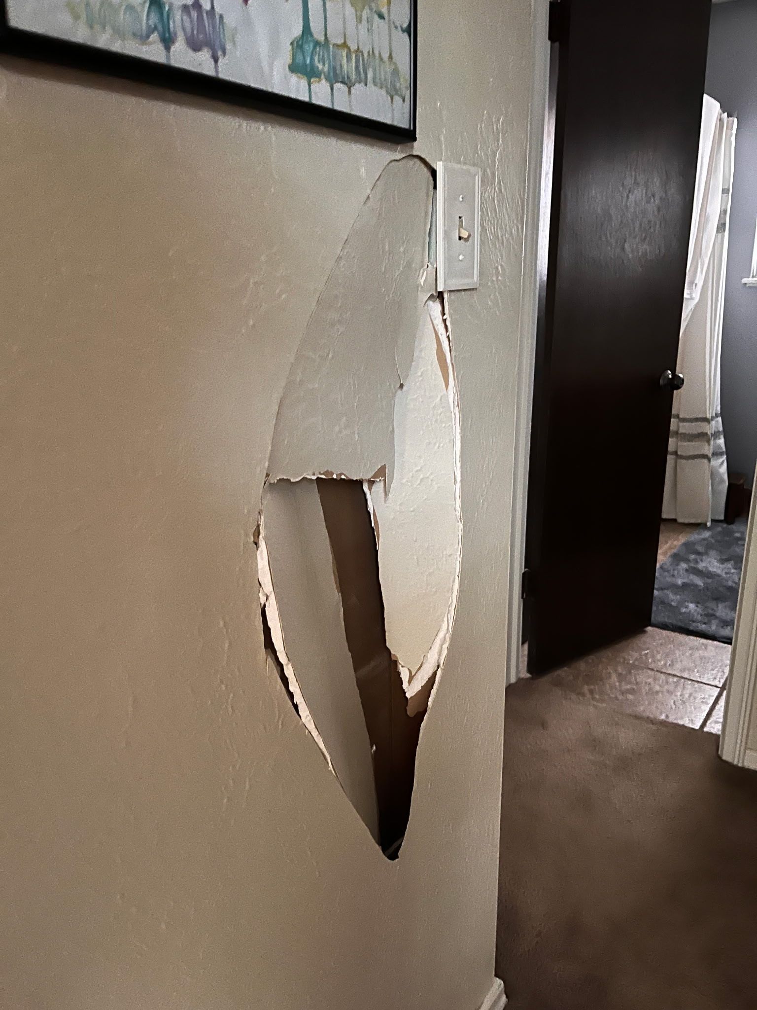 A hole in a wall in a hallway next to a door.