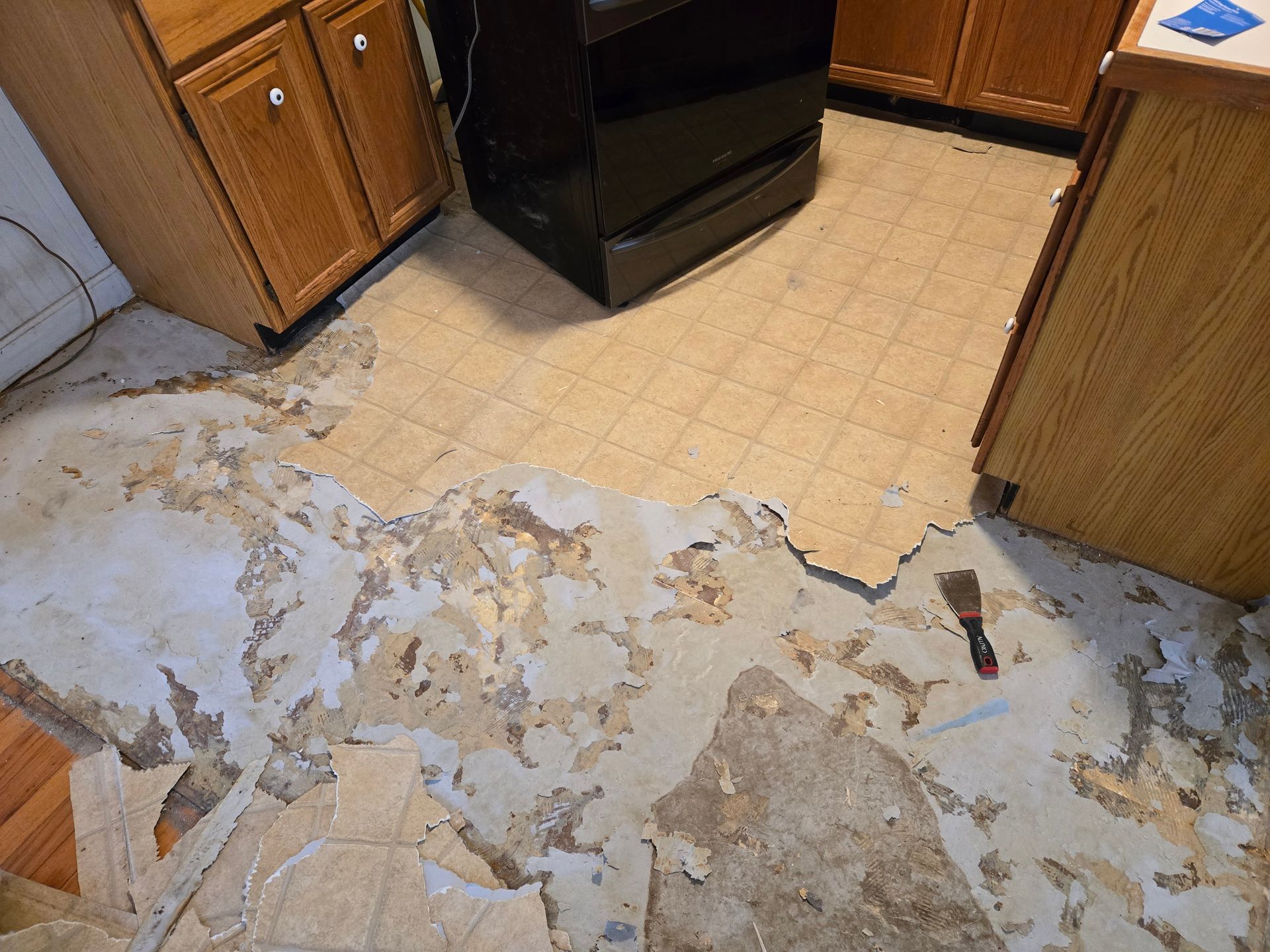 A kitchen with a stove and a spatula on the floor.