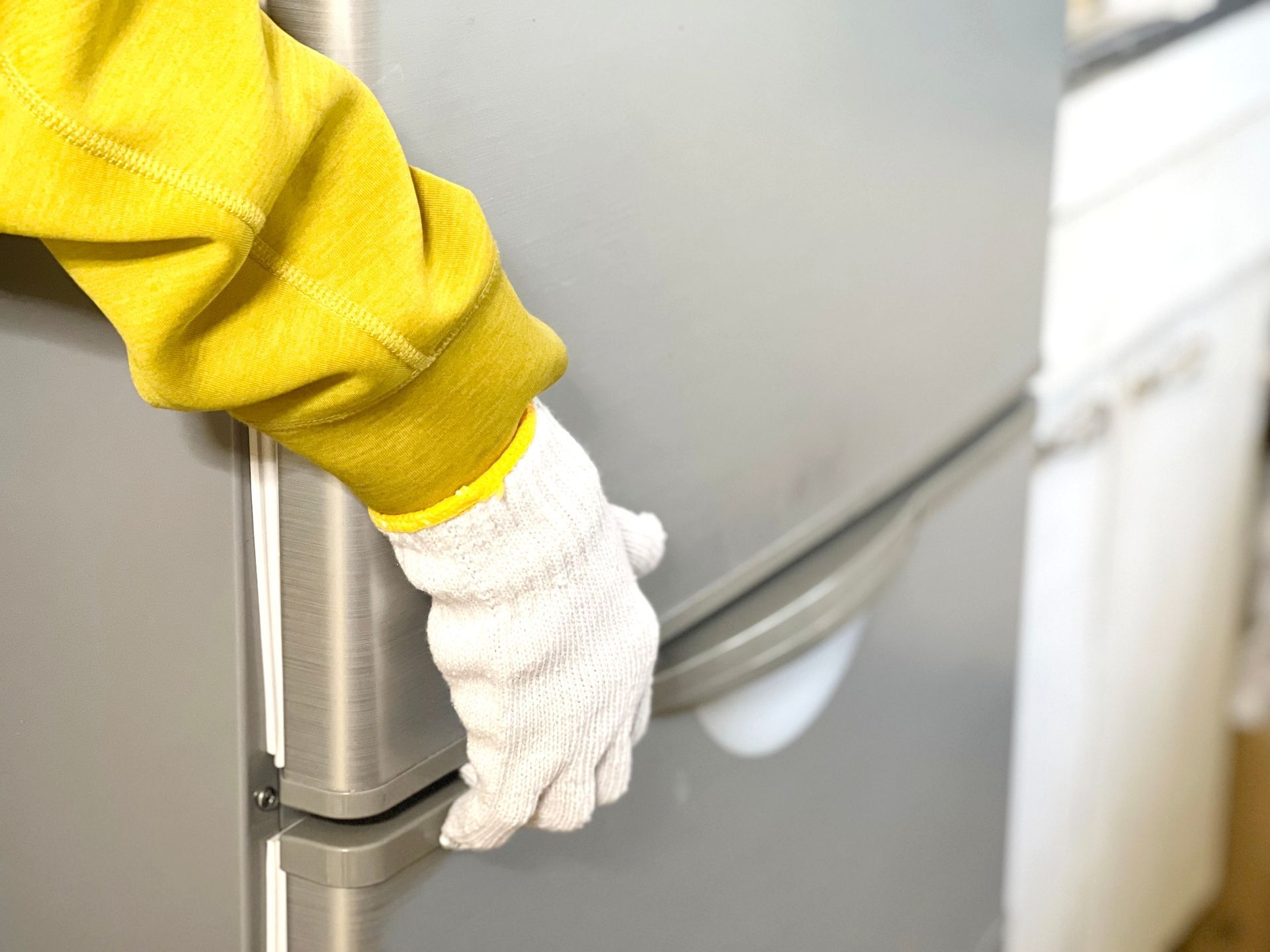 A hand wearing a white work glove grips the handle of a stainless steel refrigerator door.