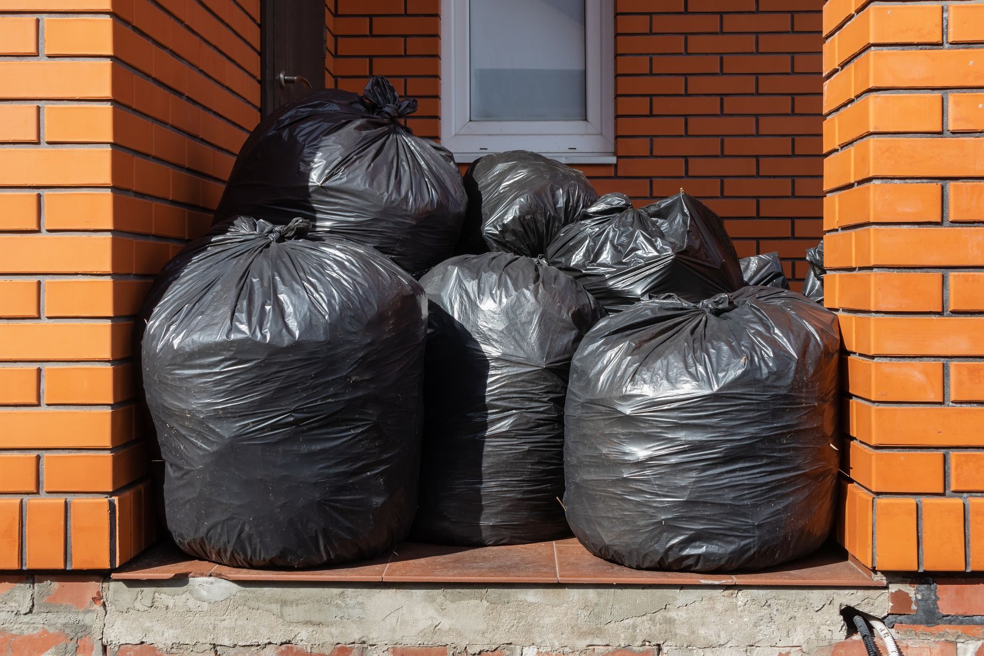 A stack of black trash bags piled up on a small landing in front of a brick building entrance.