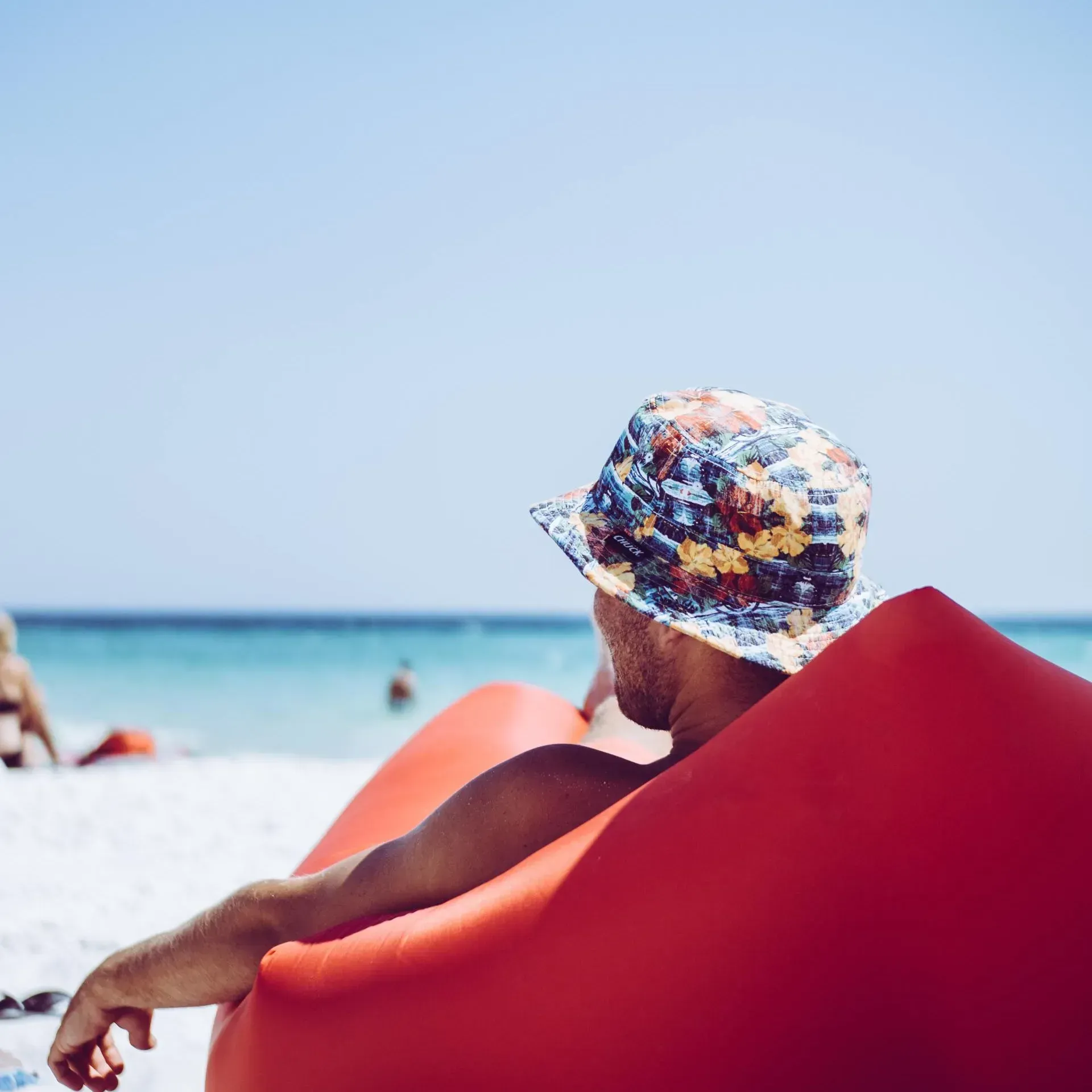 Ein Mann mit Hut sitzt auf einem roten Stuhl am Strand.