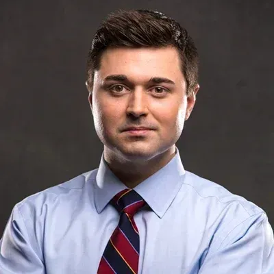 A man in a blue shirt and tie is standing with his arms crossed.