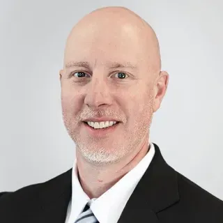 A bald man in a suit and tie is smiling for the camera.