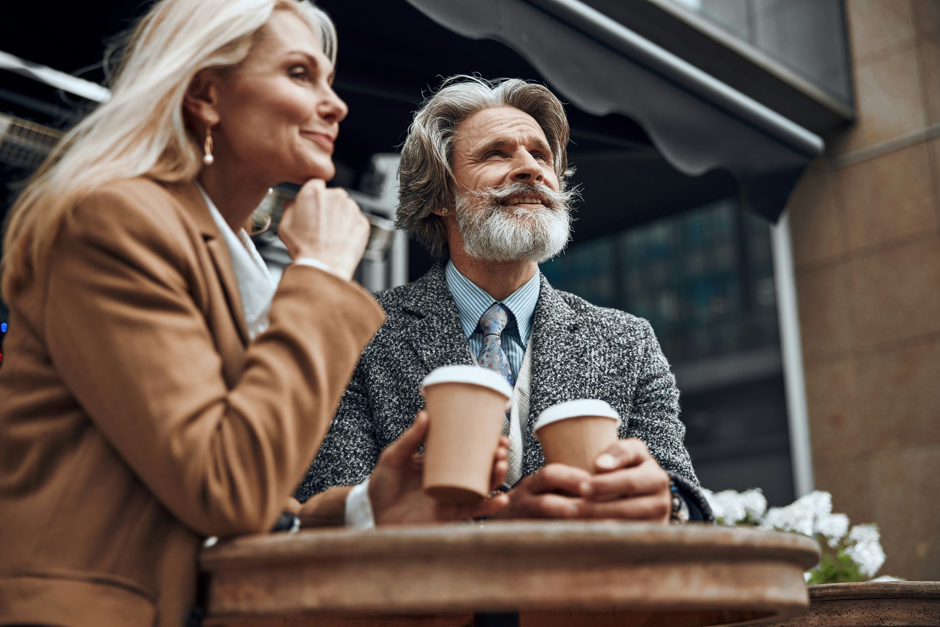 A man and a woman are sitting at a table holding cups of coffee.