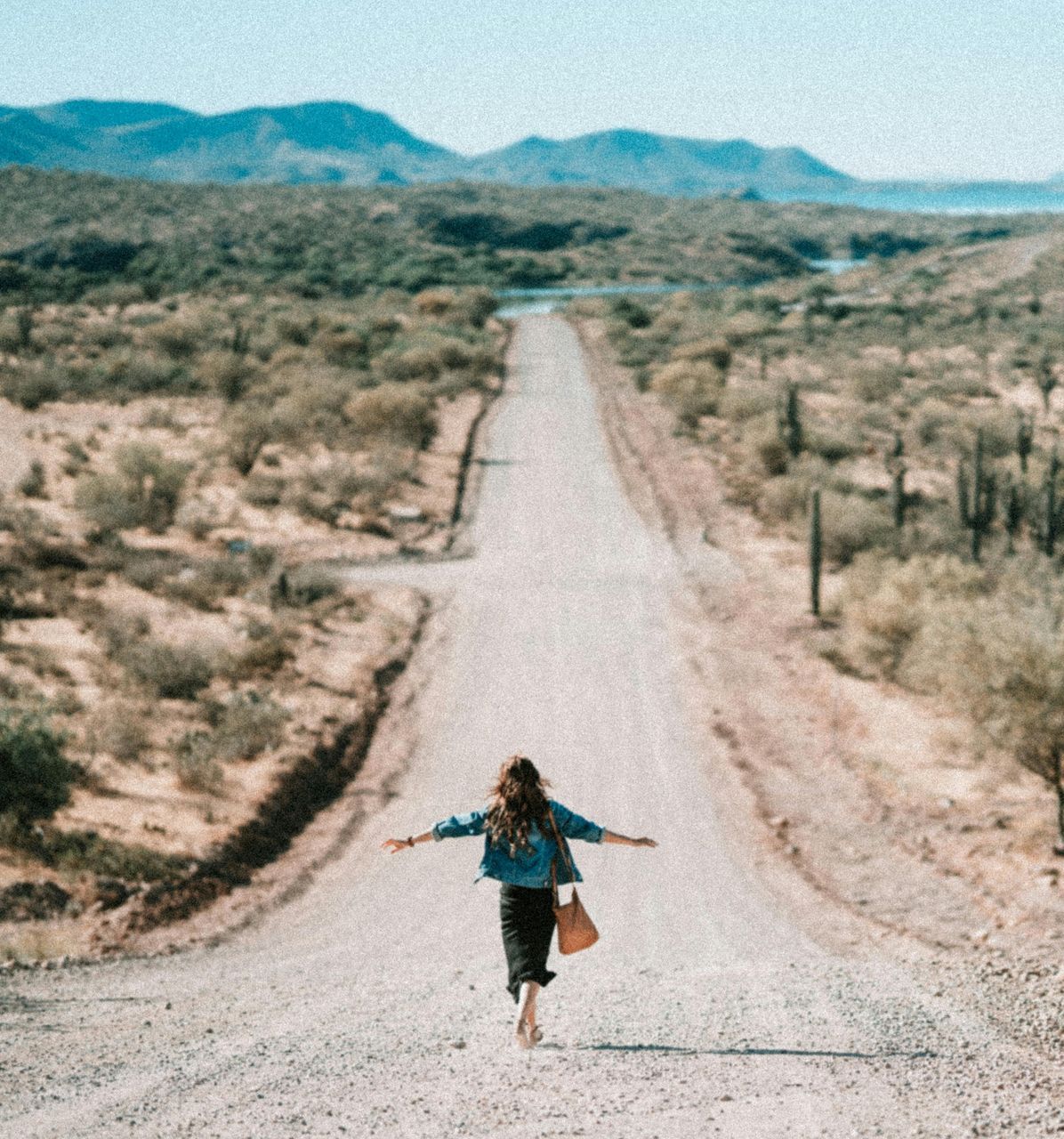 A woman is running down a dirt road with her arms outstretched