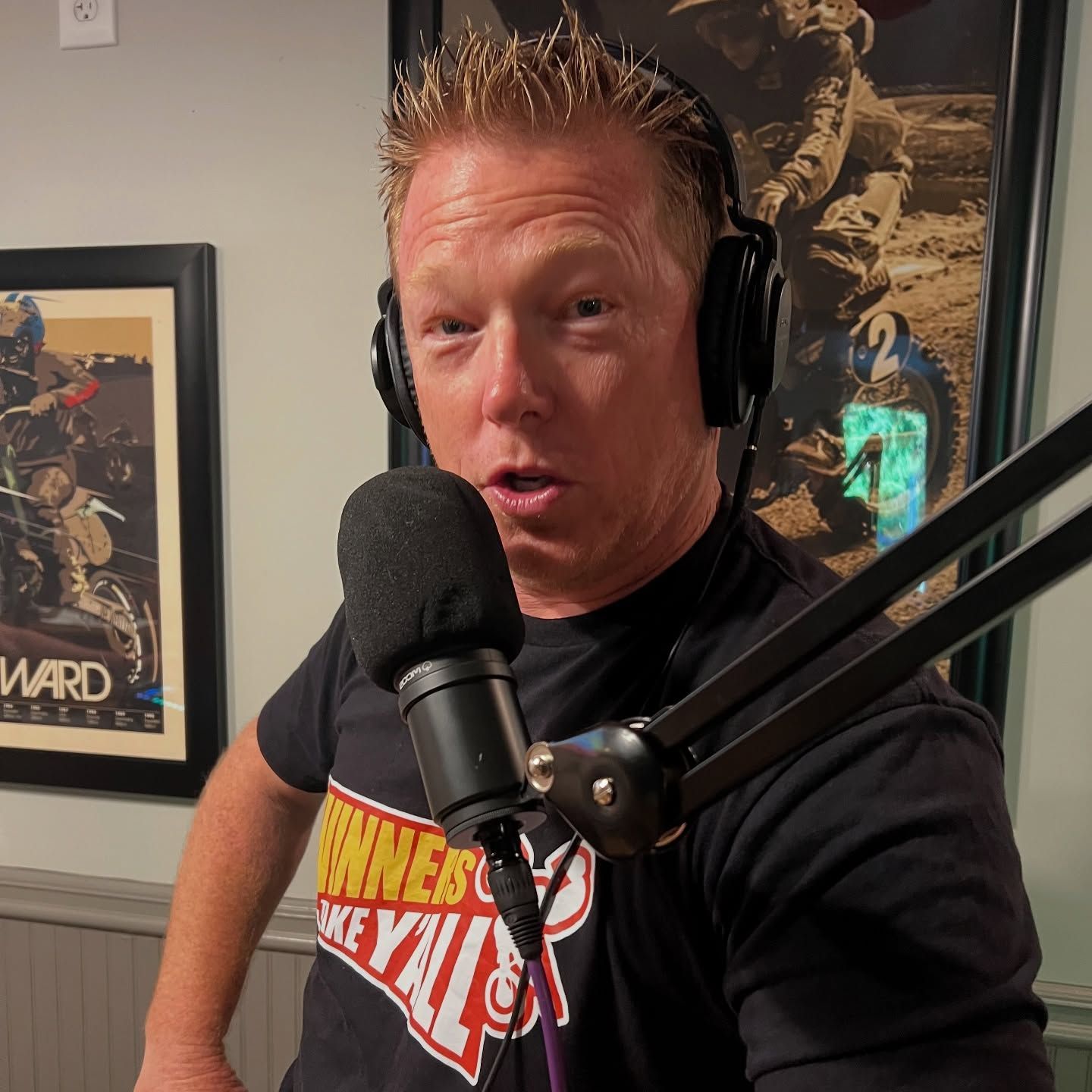 Man with headphones speaking into a microphone; indoor setting with posters.