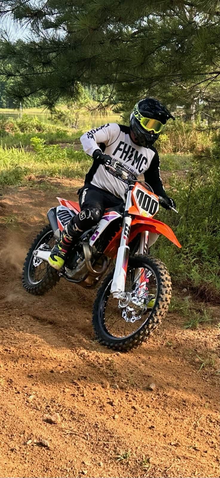 Motocross rider on an orange and white dirt bike on a dirt track, kicking up dirt.