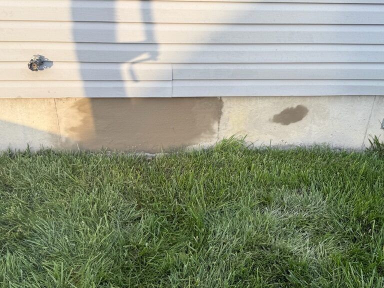 Patches of fresh concrete repair on a light-colored building foundation above a green lawn.