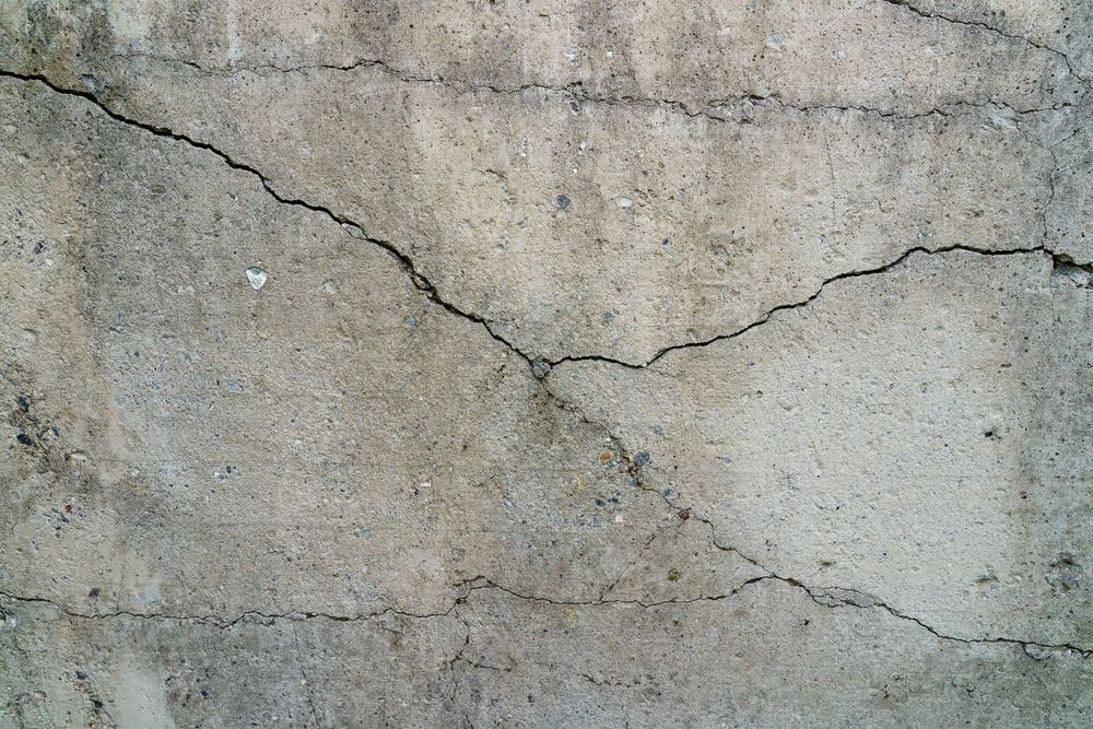 A textured, gray concrete surface featuring several prominent, branching cracks spreading across the middle.