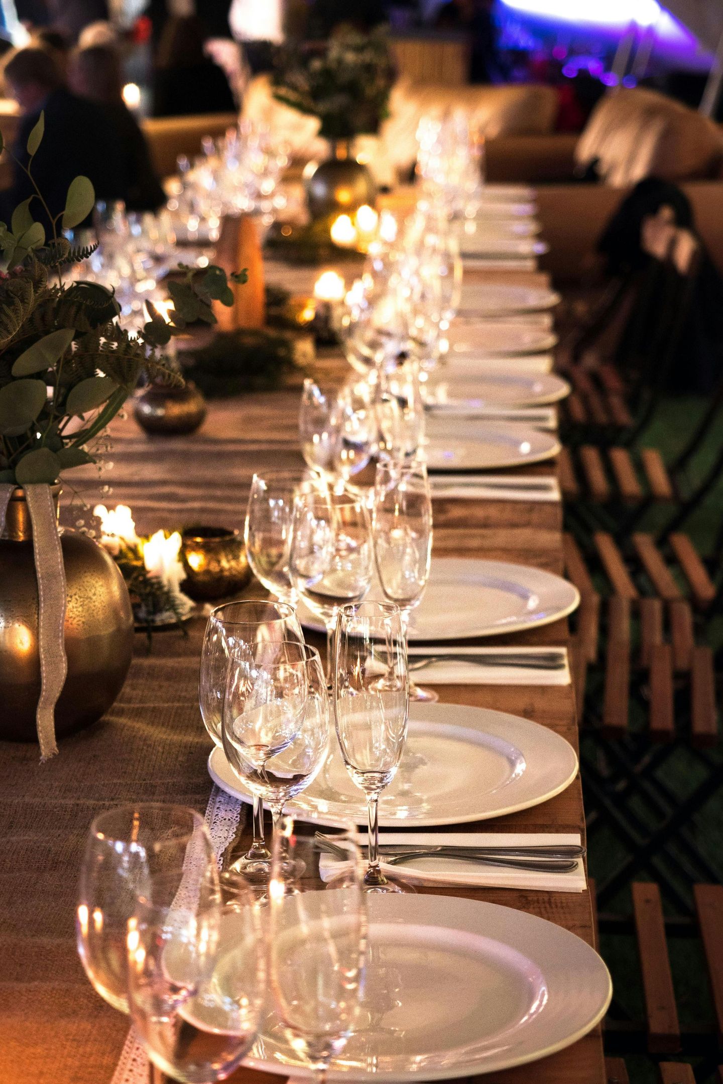 Long dining table set for a formal event with white plates, crystal glasses, and candles.