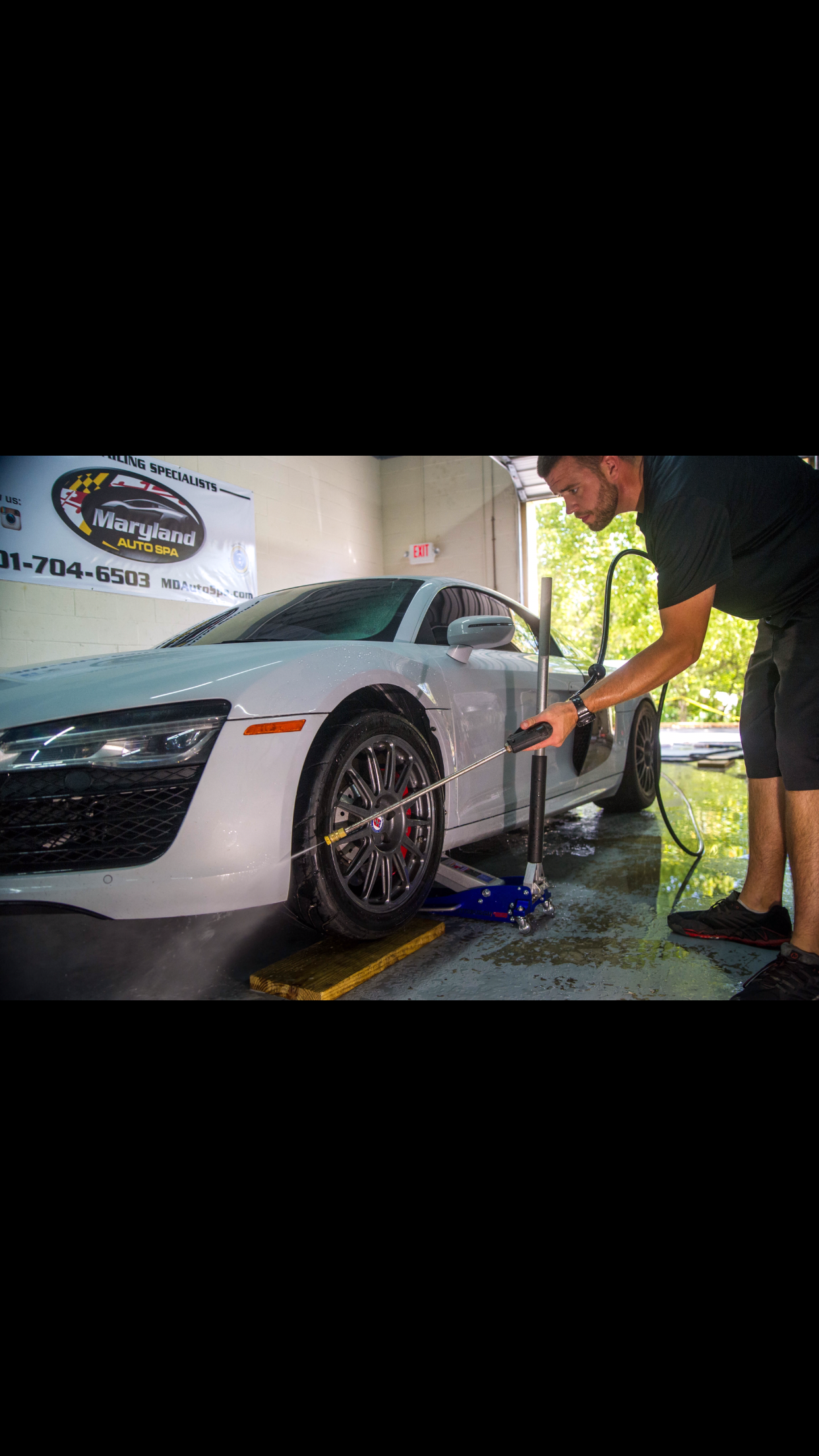A man is washing a white car in a garage.