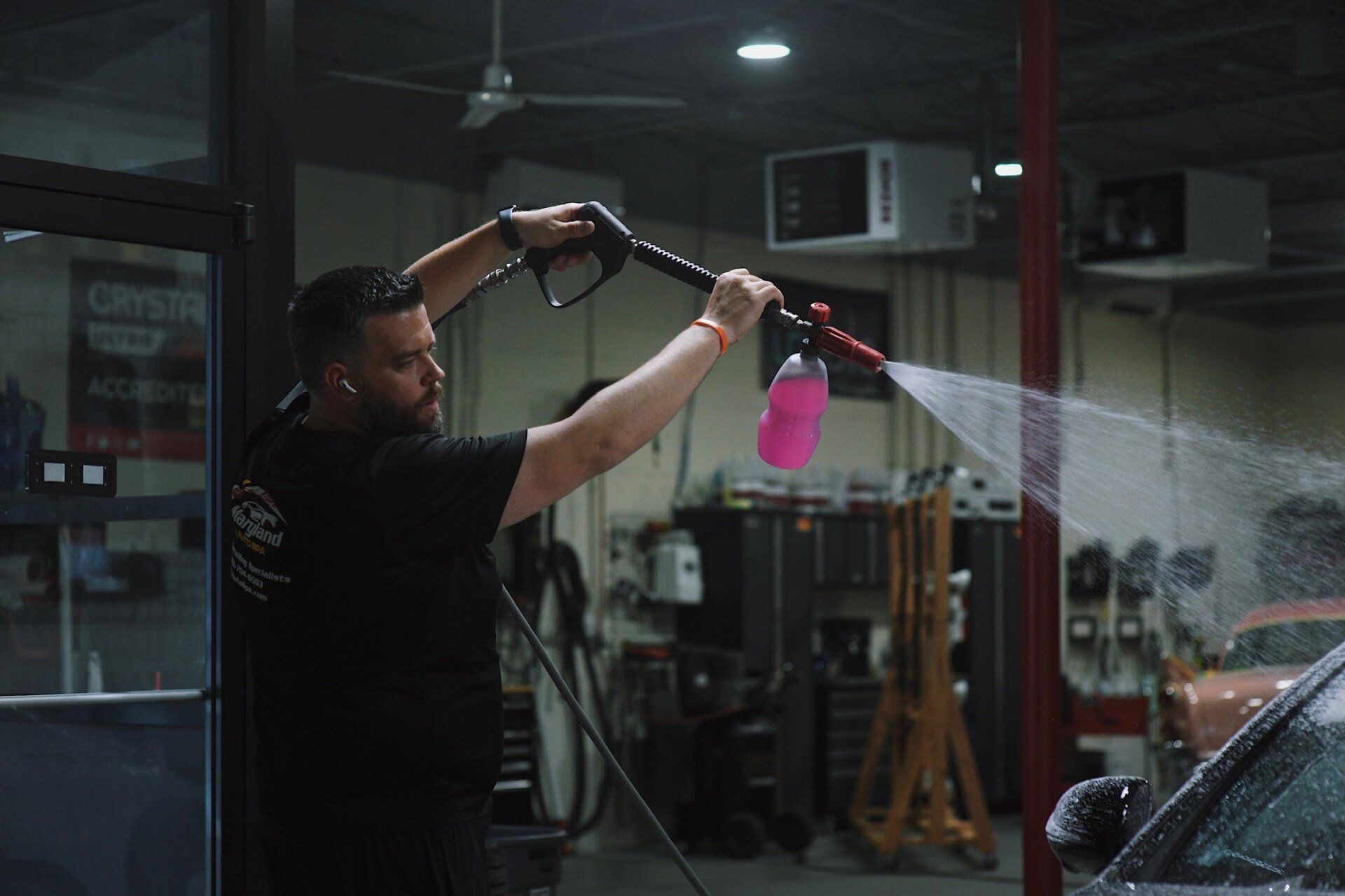 A man is washing a car with a high pressure washer in a garage.