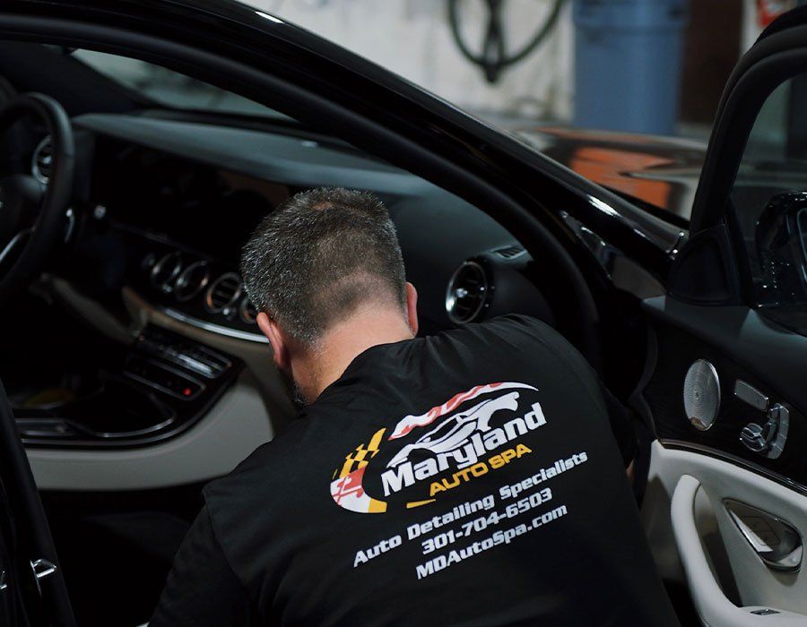 A man in a maryland auto spa shirt is working on a car