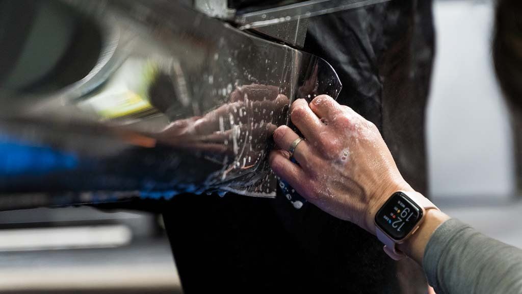 A person wearing an apple watch is cleaning a car with a cloth.