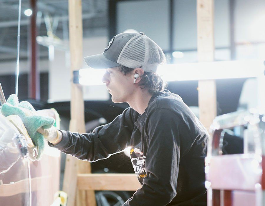 A man wearing a hat is cleaning a car with a cloth.
