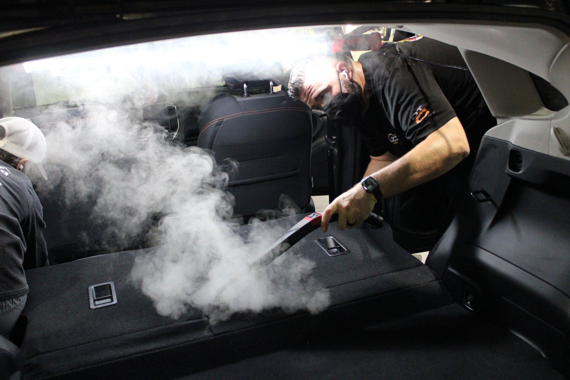 A man is cleaning the back seat of a car with a steam cleaner.