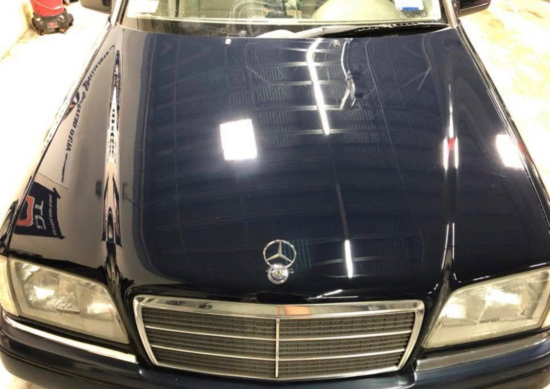 A black mercedes is parked in a garage with the hood up