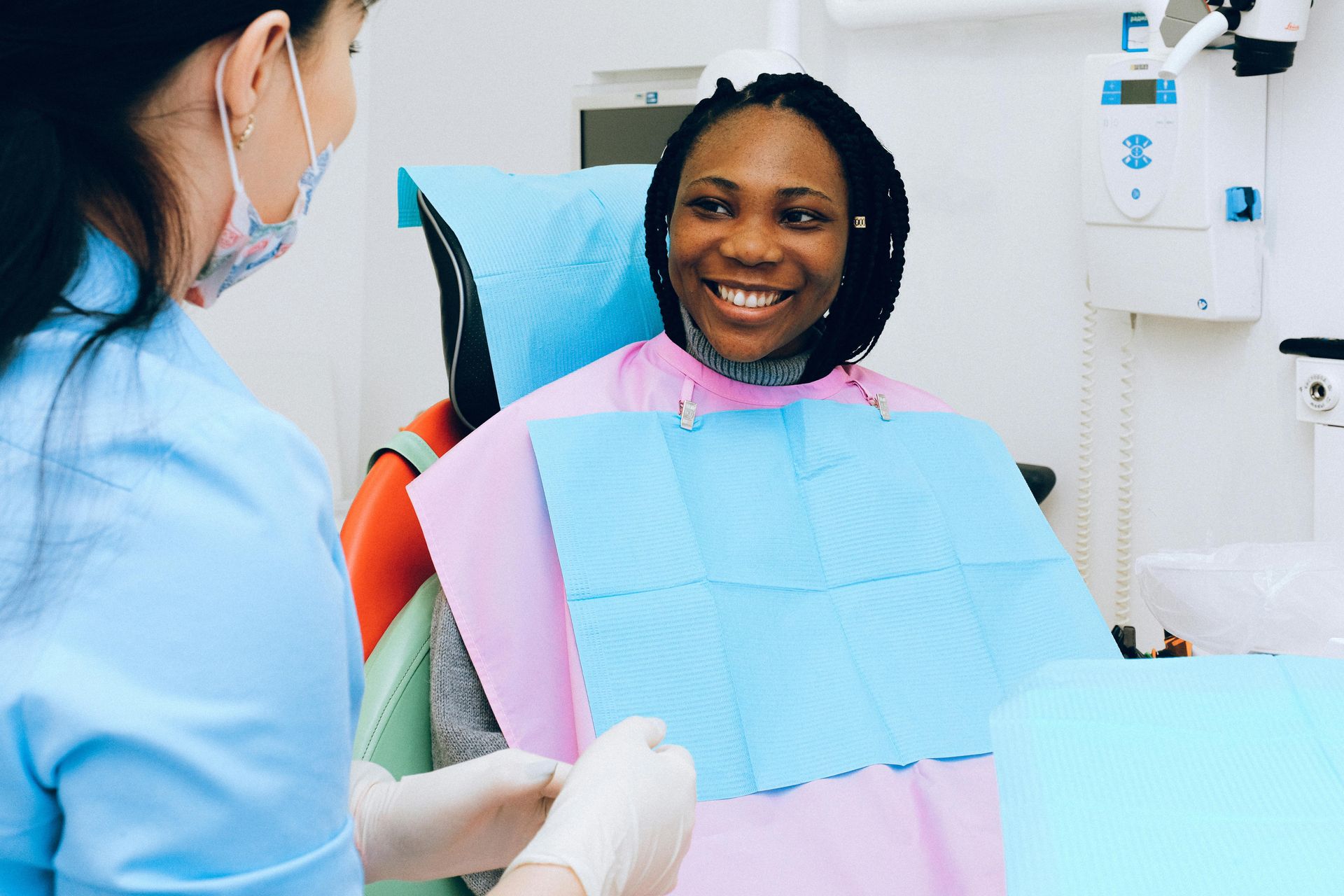 Woman in dental chair smiles at dentist, who wears a mask and gloves.