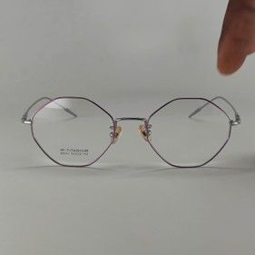Silver-rimmed, geometric octagonal eyeglasses on a plain background, held by a person's finger.