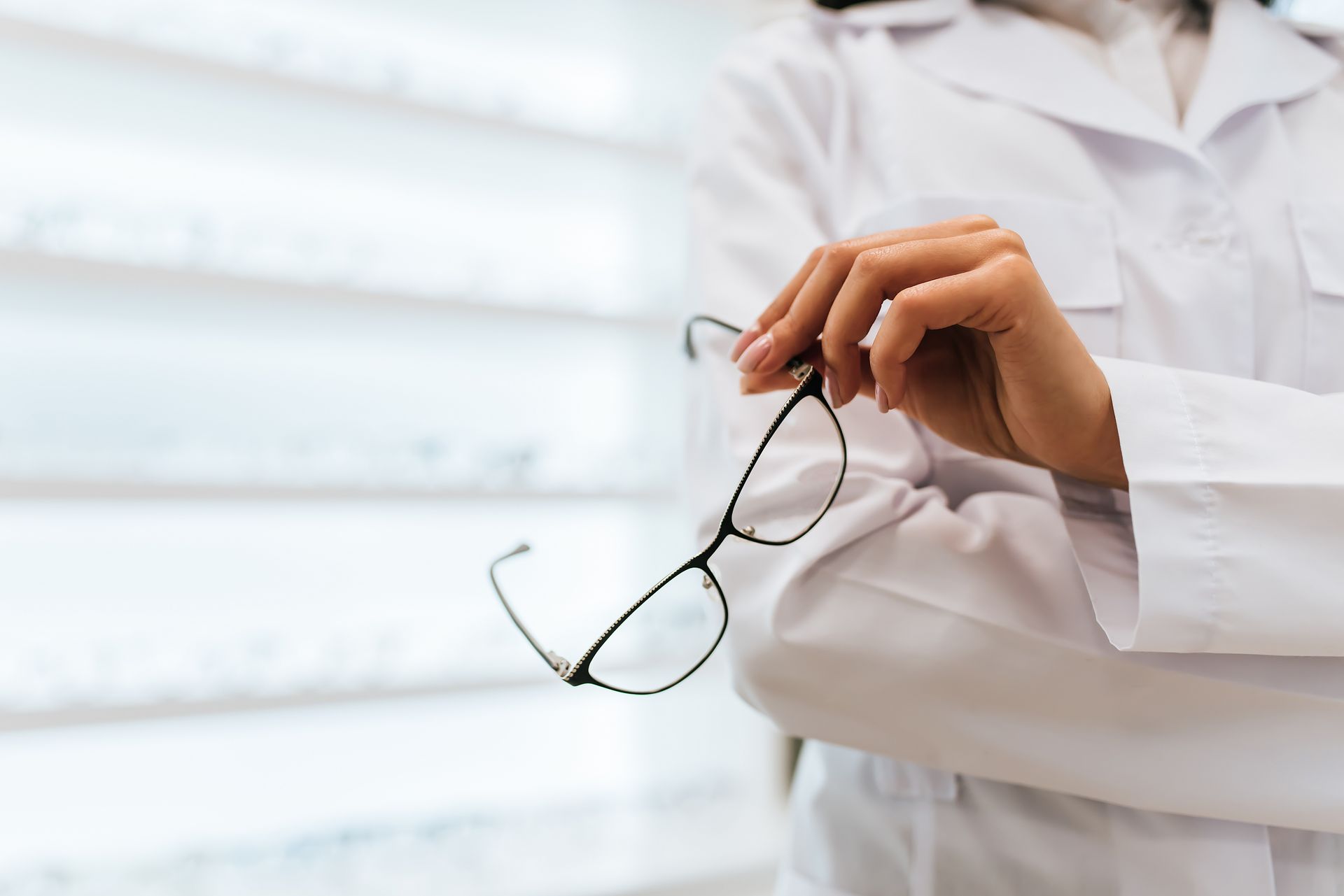 Person in a white lab coat holding eyeglasses in an optical store.