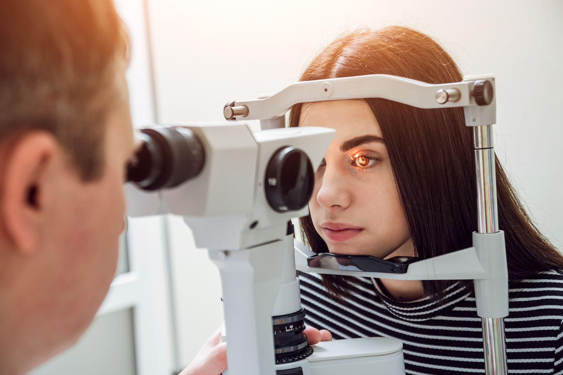 Optometrist examining a patient's eye with a slit lamp in a clinic.