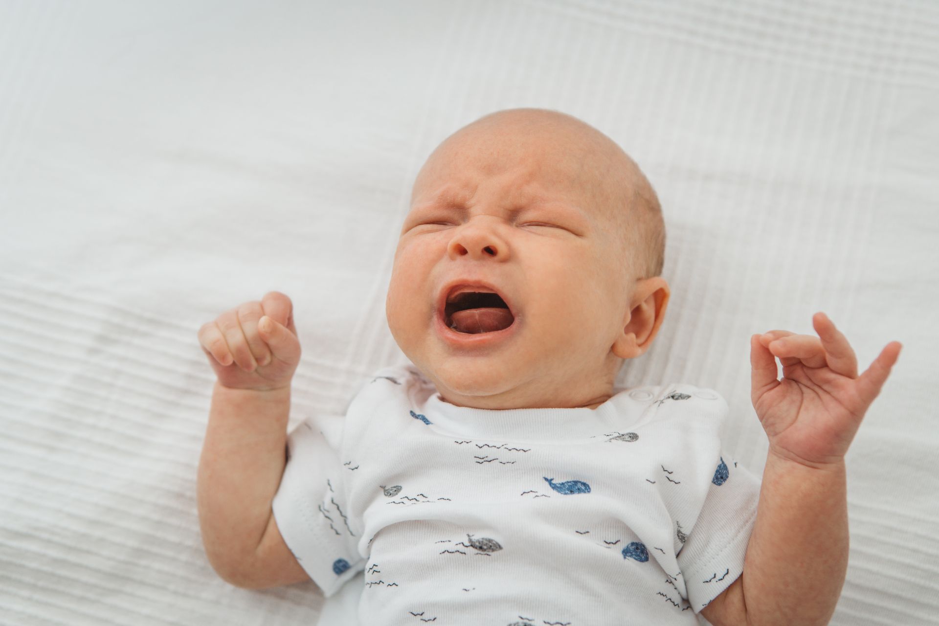 A baby is crying while laying on a bed.