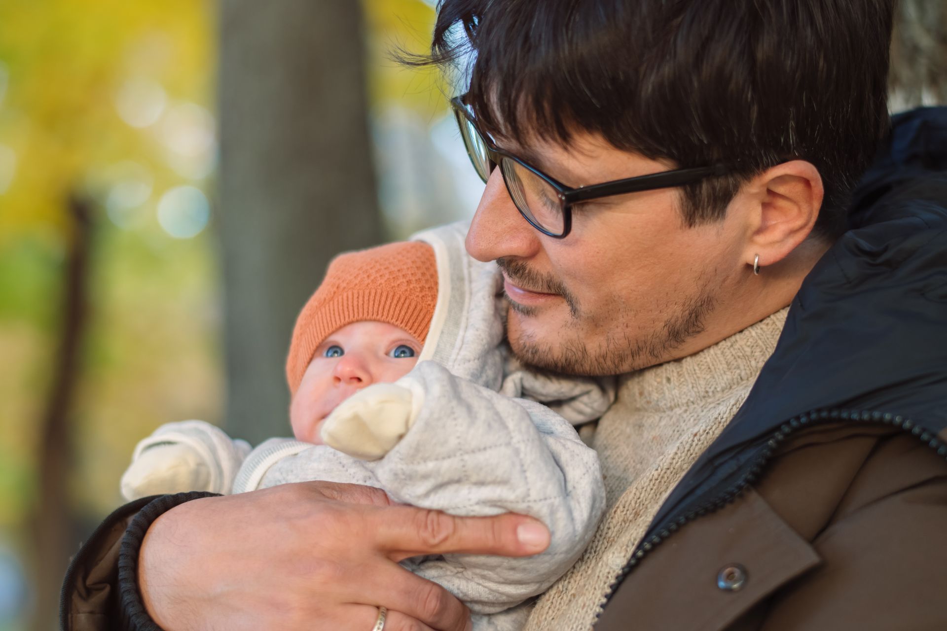 A man wearing glasses is holding a baby in his arms.