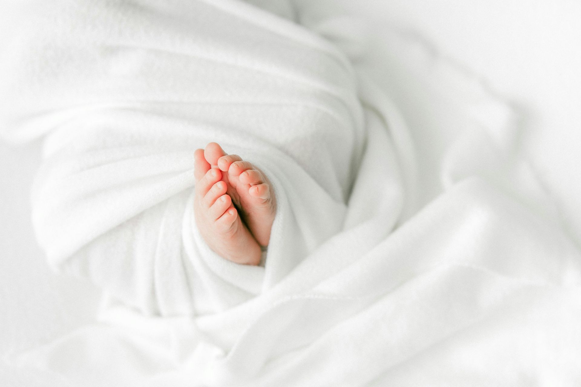 Baby feet peeking out from soft, white blanket.