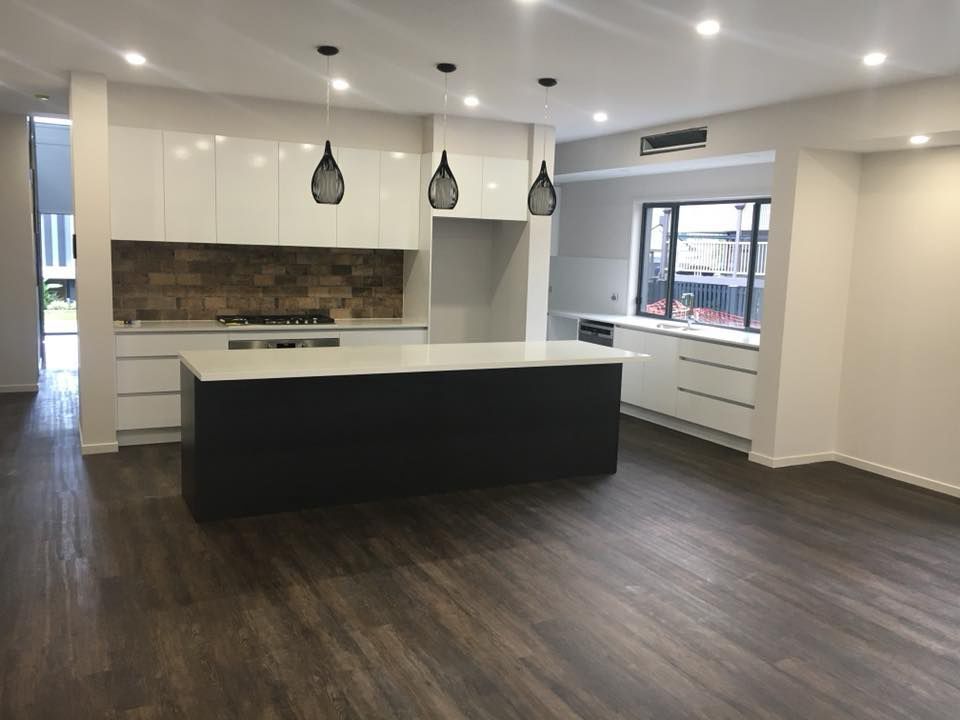 An Empty Kitchen with White Cabinets and A Large Island — Polson Construction in Kedron, QLD