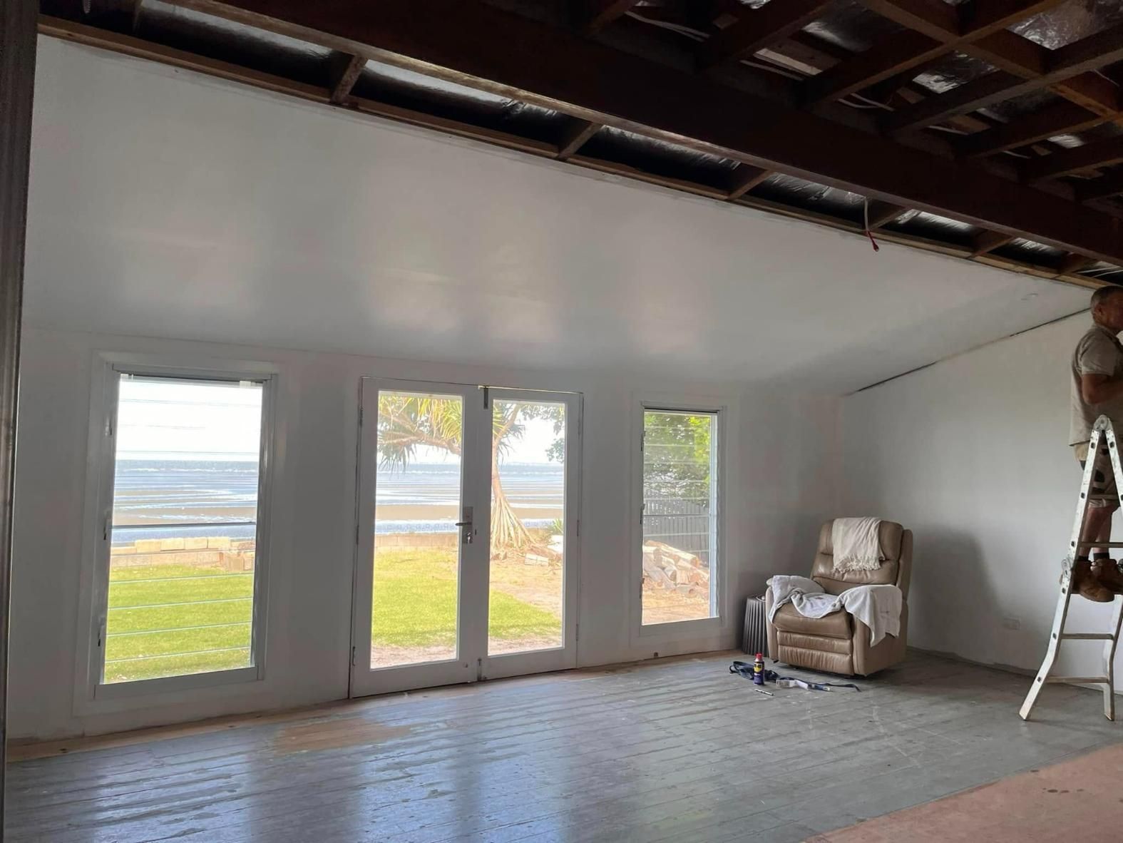 A Man Is Standing on A Ladder in A Room with A Lot of Windows — Polson Construction in Kedron, QLD