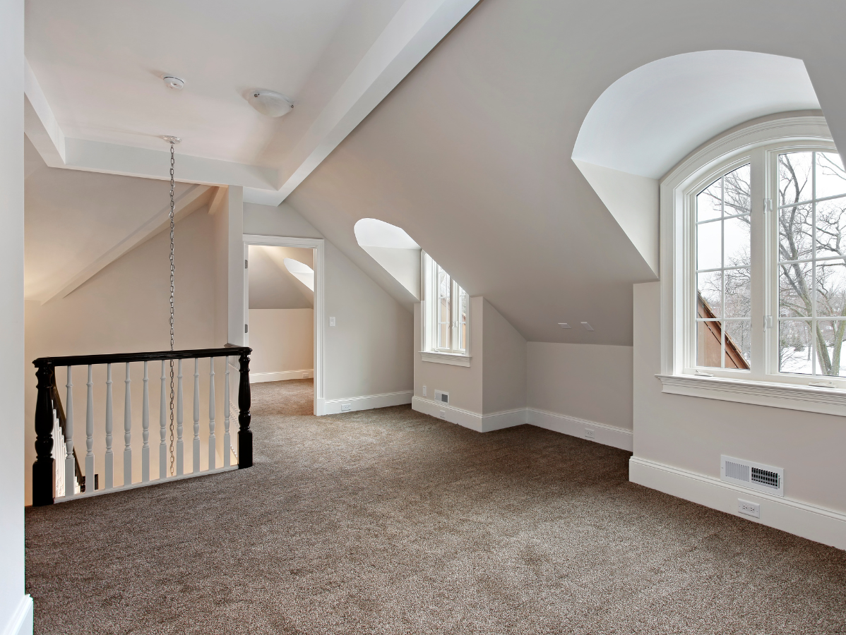 Attic room with neutral carpet, arched windows, and a staircase.